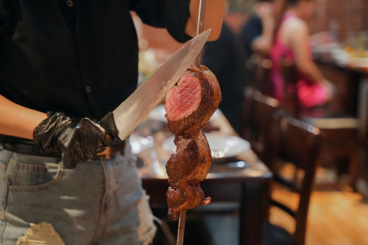 A Brasa passador carving a slice of beef from a long skewer at the table
