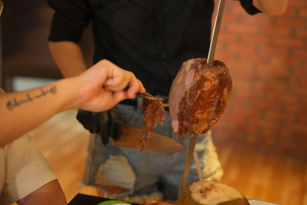 A Brasa passador serving a slice of beef from a skewer to a guest at the table