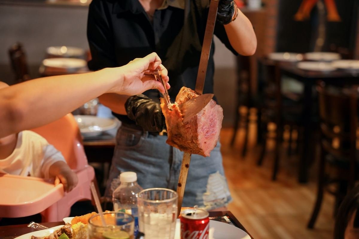 A passador serving beef from a skewer to a guest during rodízio at Brasa